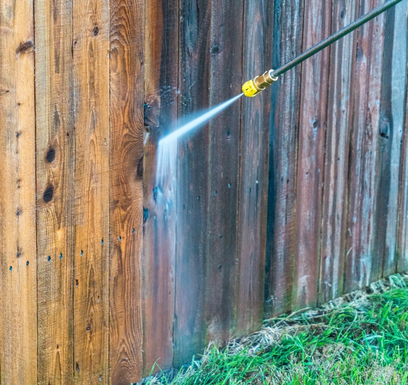 A wooden fence being cleaned with a pressure washer, removing dirt and discoloration.