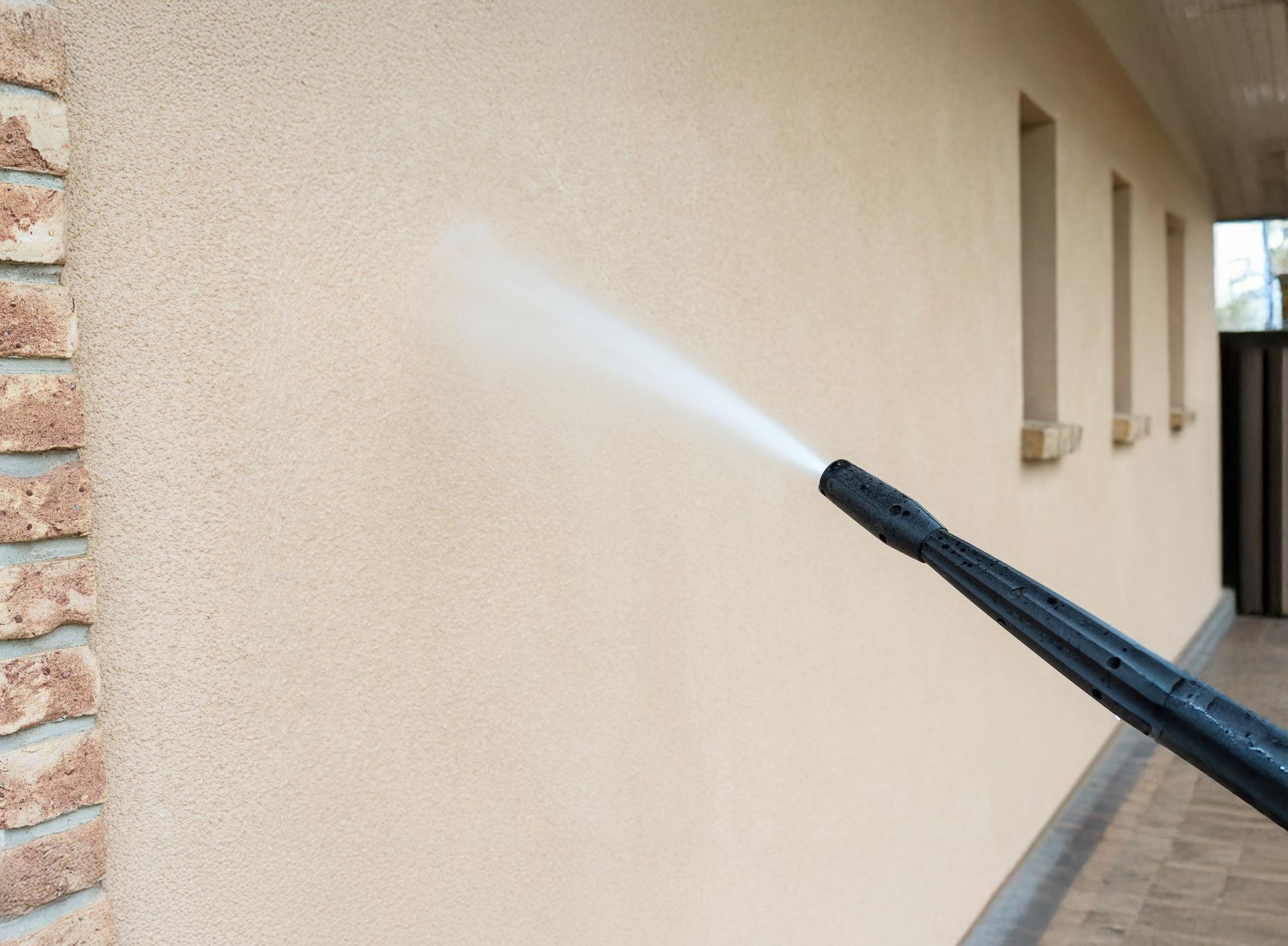 Pressure washer cleaning a light beige stucco wall outside.