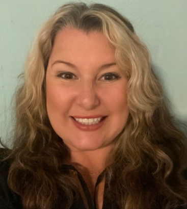Woman with long, wavy brown and blonde hair, smiling.  Wearing a black shirt, against a light blue background.