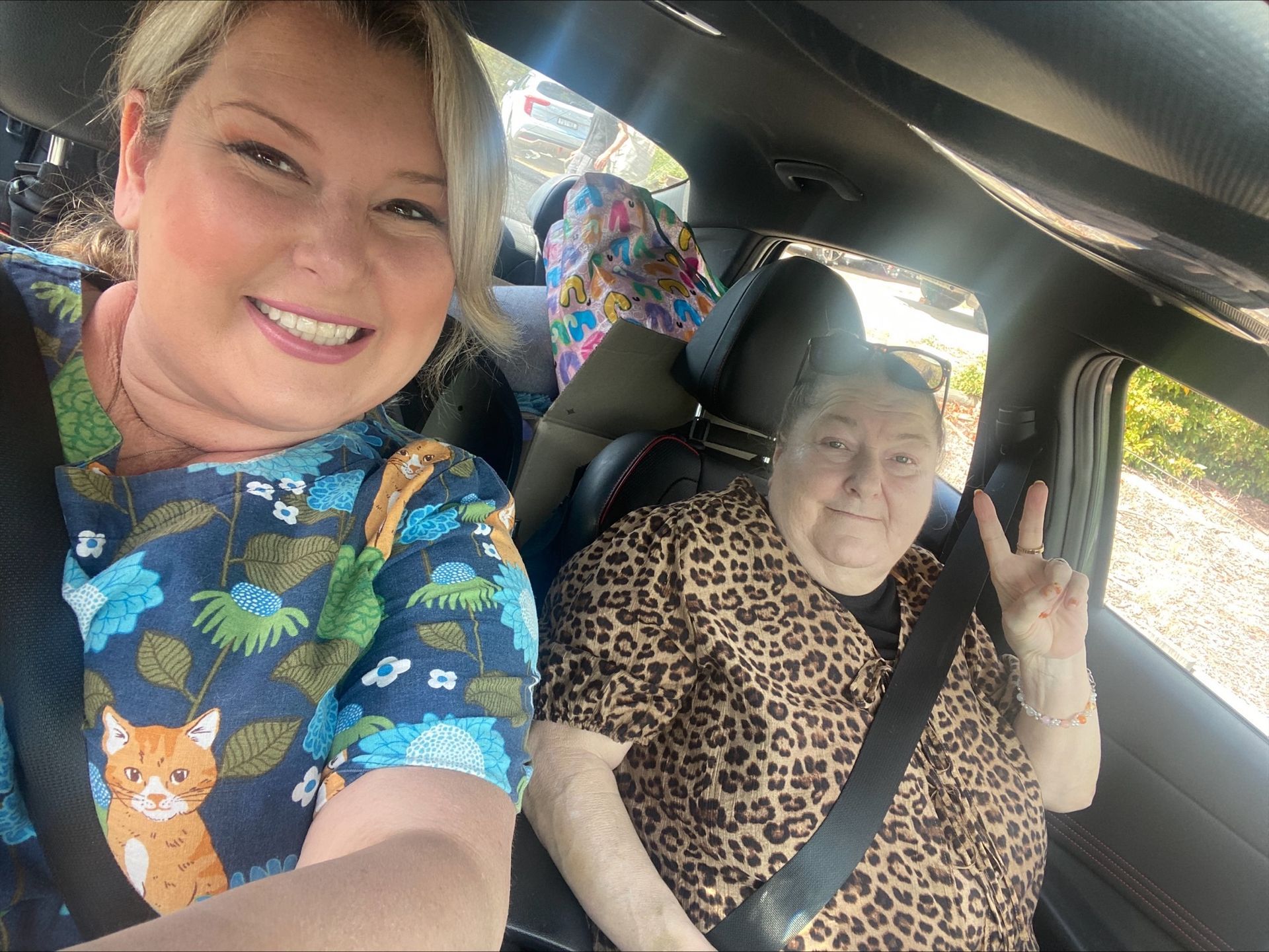 Person putting a blue coat on a black dog on a concrete surface next to plants.