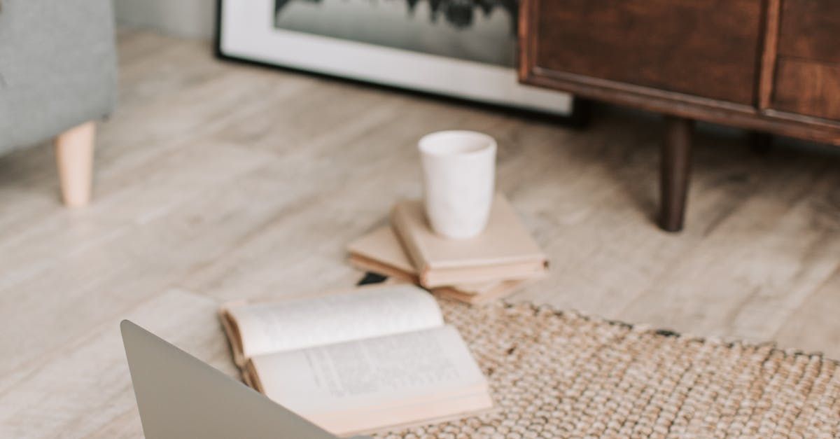 A laptop is sitting on a rug next to a book and a cup of coffee.