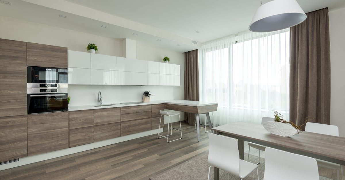 A kitchen with wooden cabinets and white counter tops and a dining table and chairs.