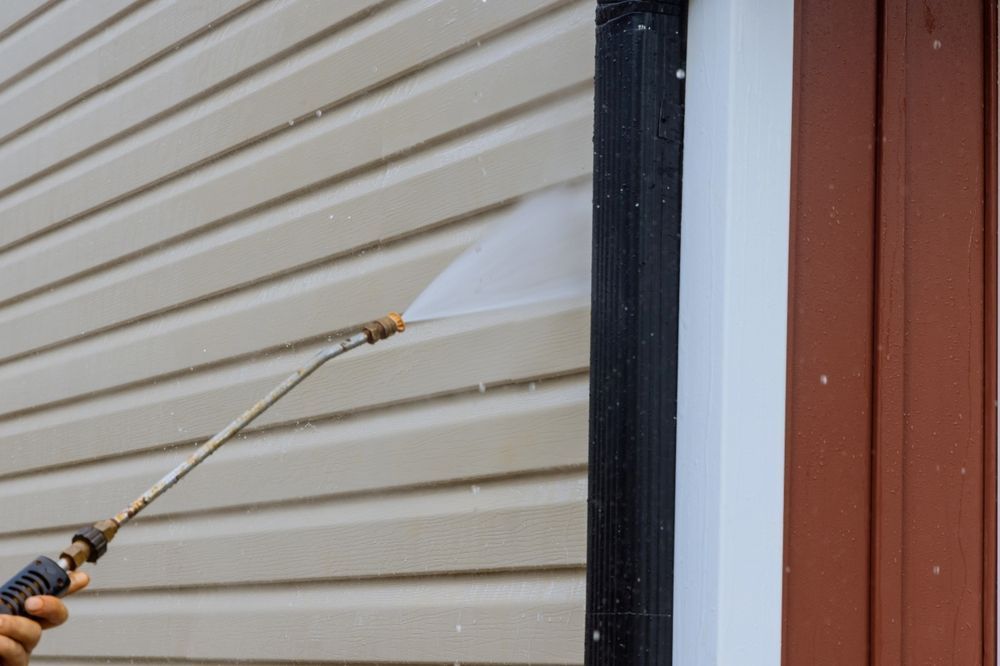 Yellow pressure washer cleaning a wet concrete surface beside a driveway edge