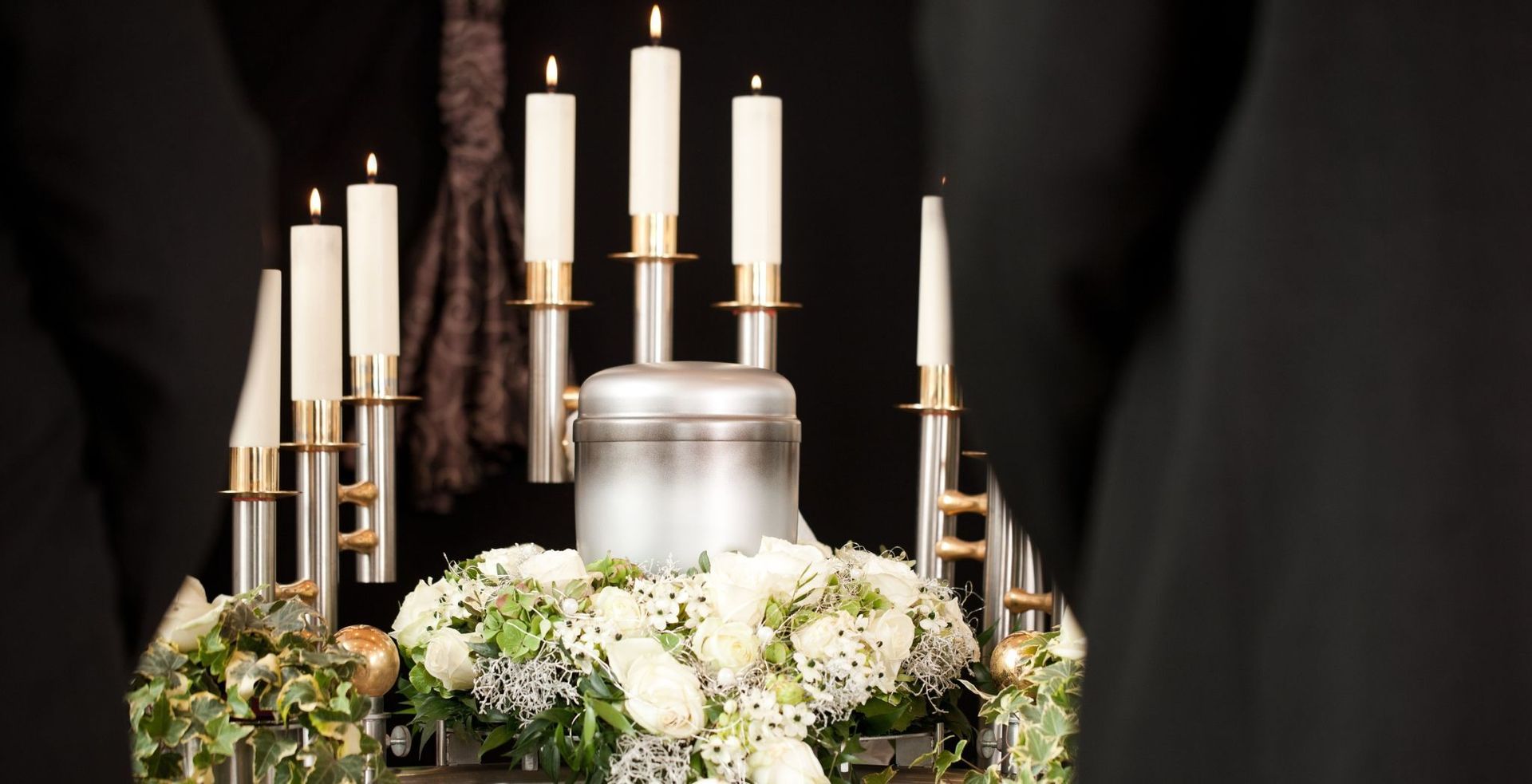 Wooden casket with floral arrangement, in a church with flags and more flowers.
