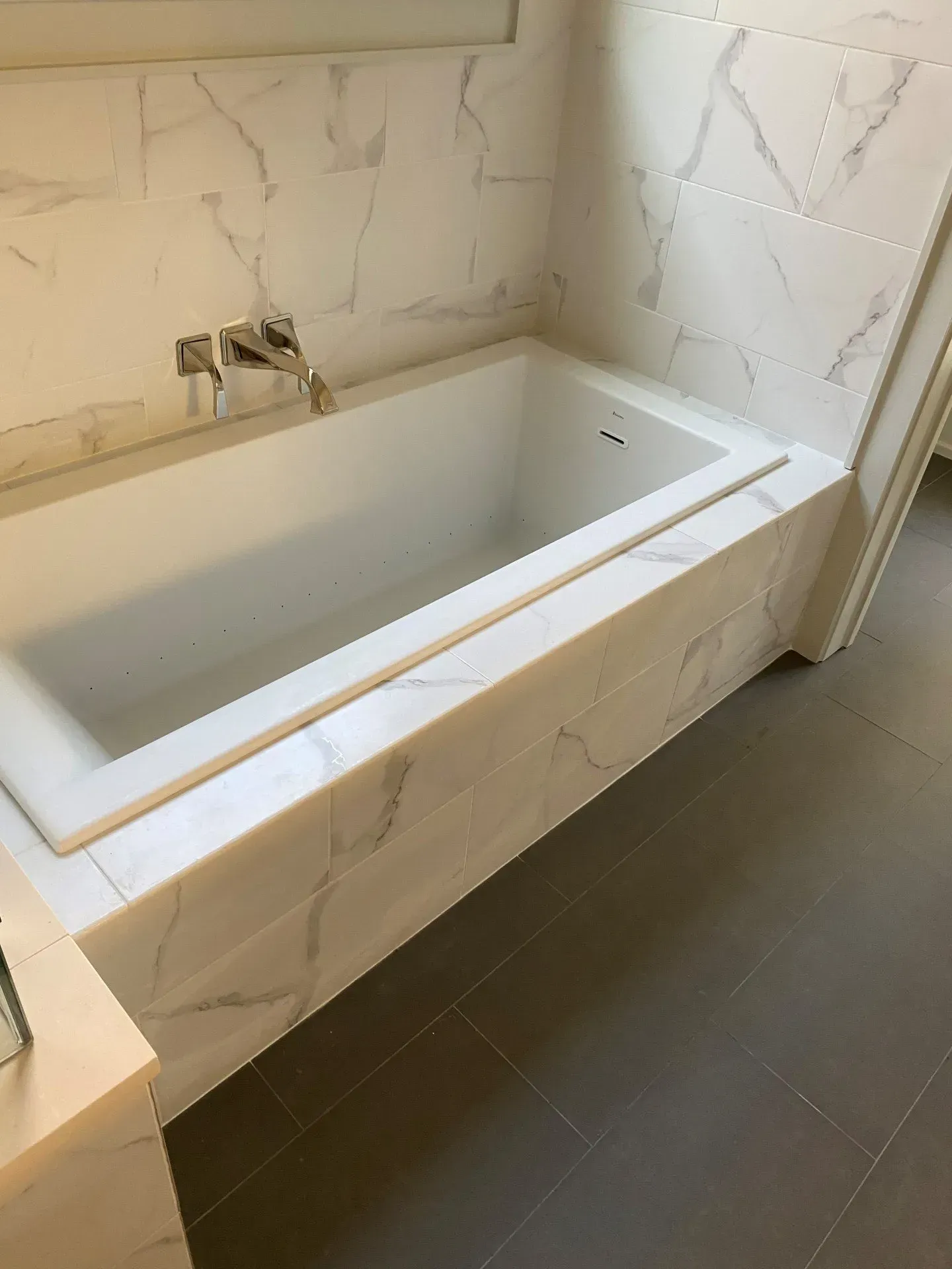 A bathtub in a bathroom with marble tiles on the wall and floor