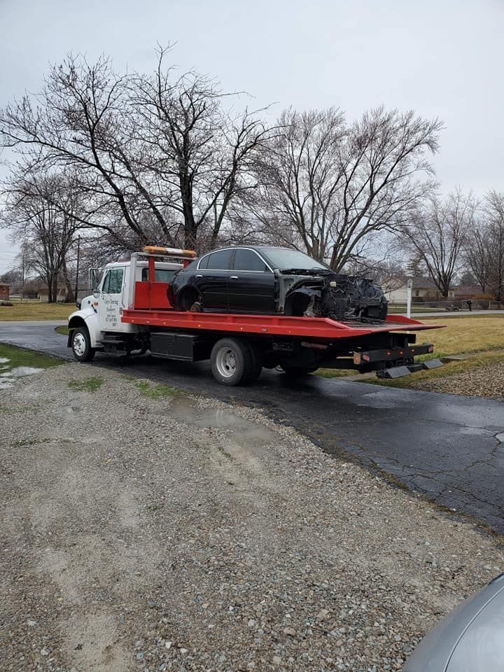 A tow truck is carrying a black car on the back of it.