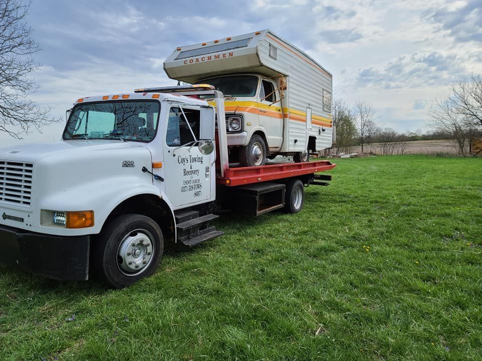 A tow truck is carrying a camper on top of it.