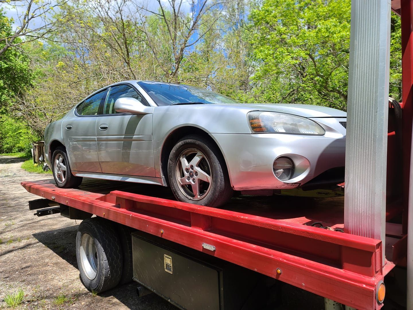 A silver car is sitting on top of a red tow truck.