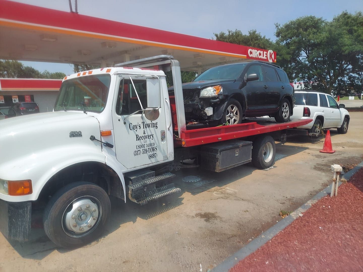 A tow truck with two cars on the back is parked in front of a gas station.