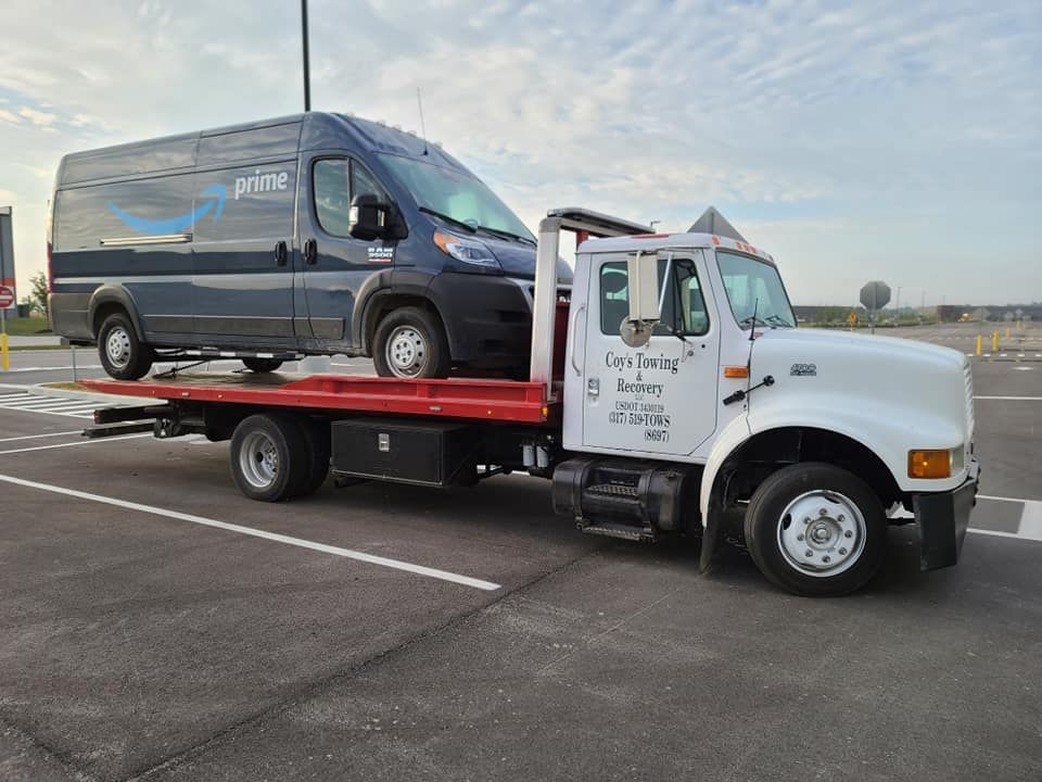 A tow truck is towing a van in a parking lot.