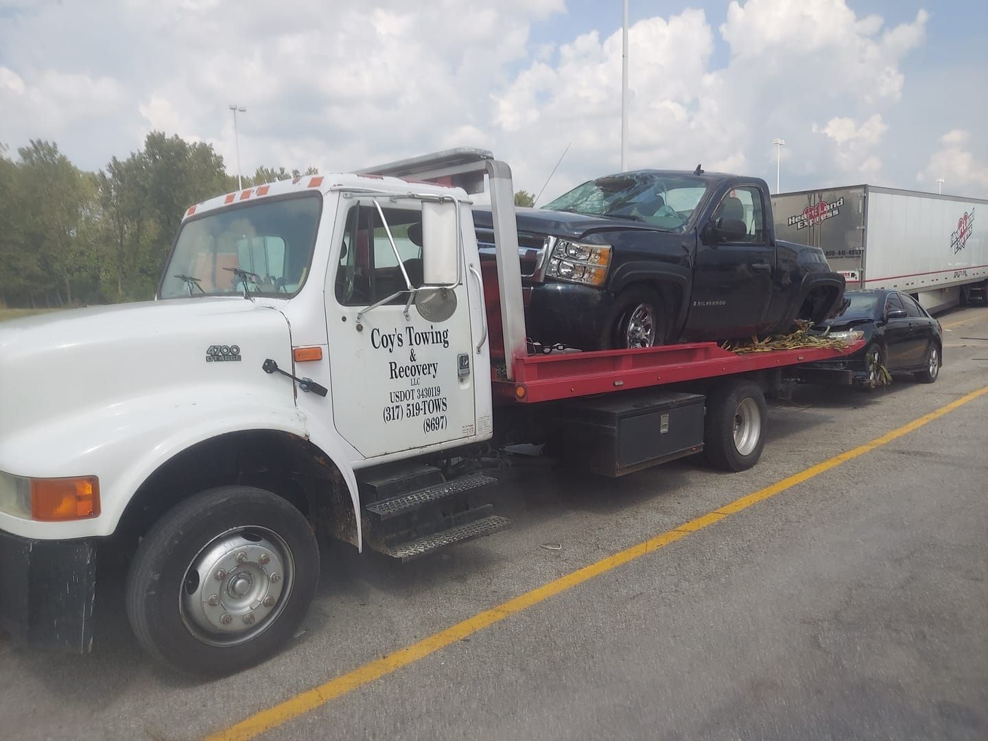A tow truck with two cars on the back is parked on the side of the road.
