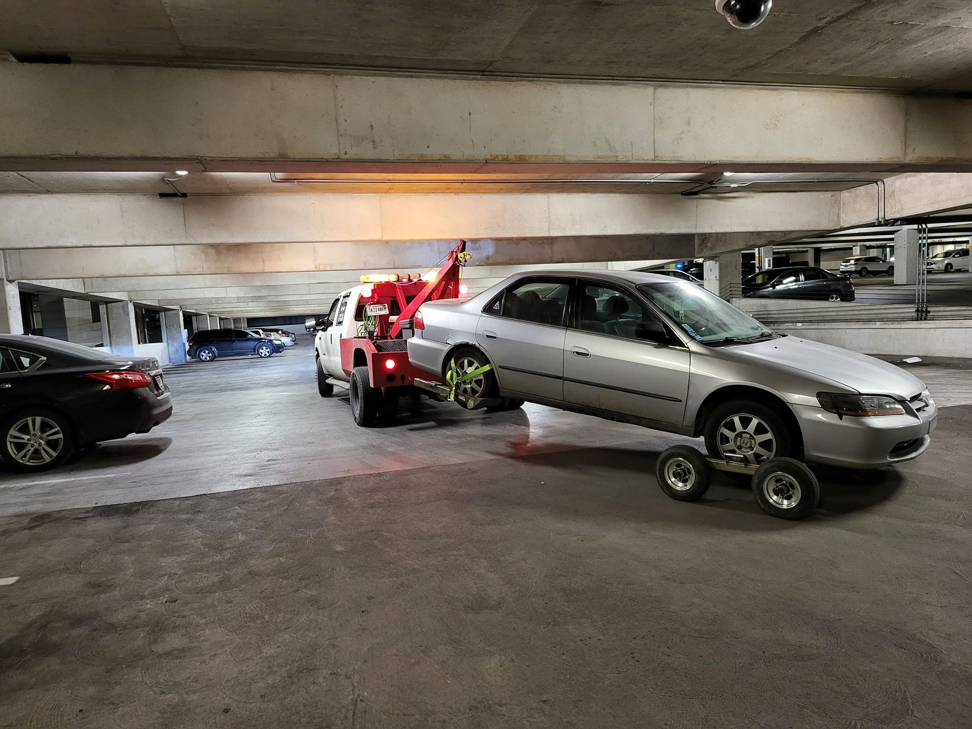 A silver car is being towed by a tow truck in a parking garage.
