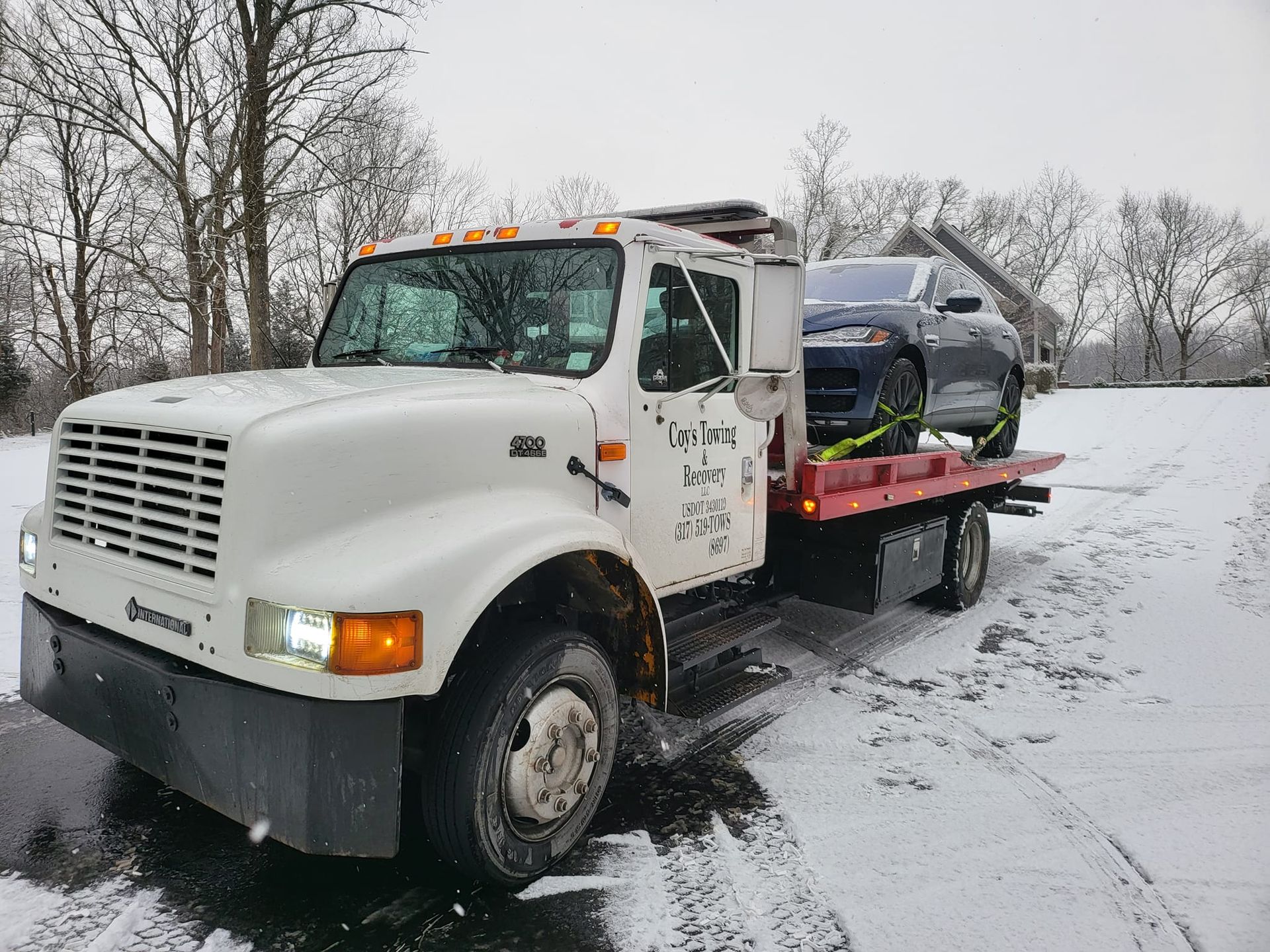 A tow truck is towing a car in the snow.