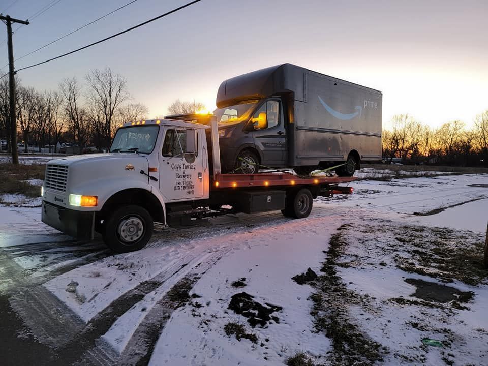 A tow truck is towing a delivery truck in the snow.