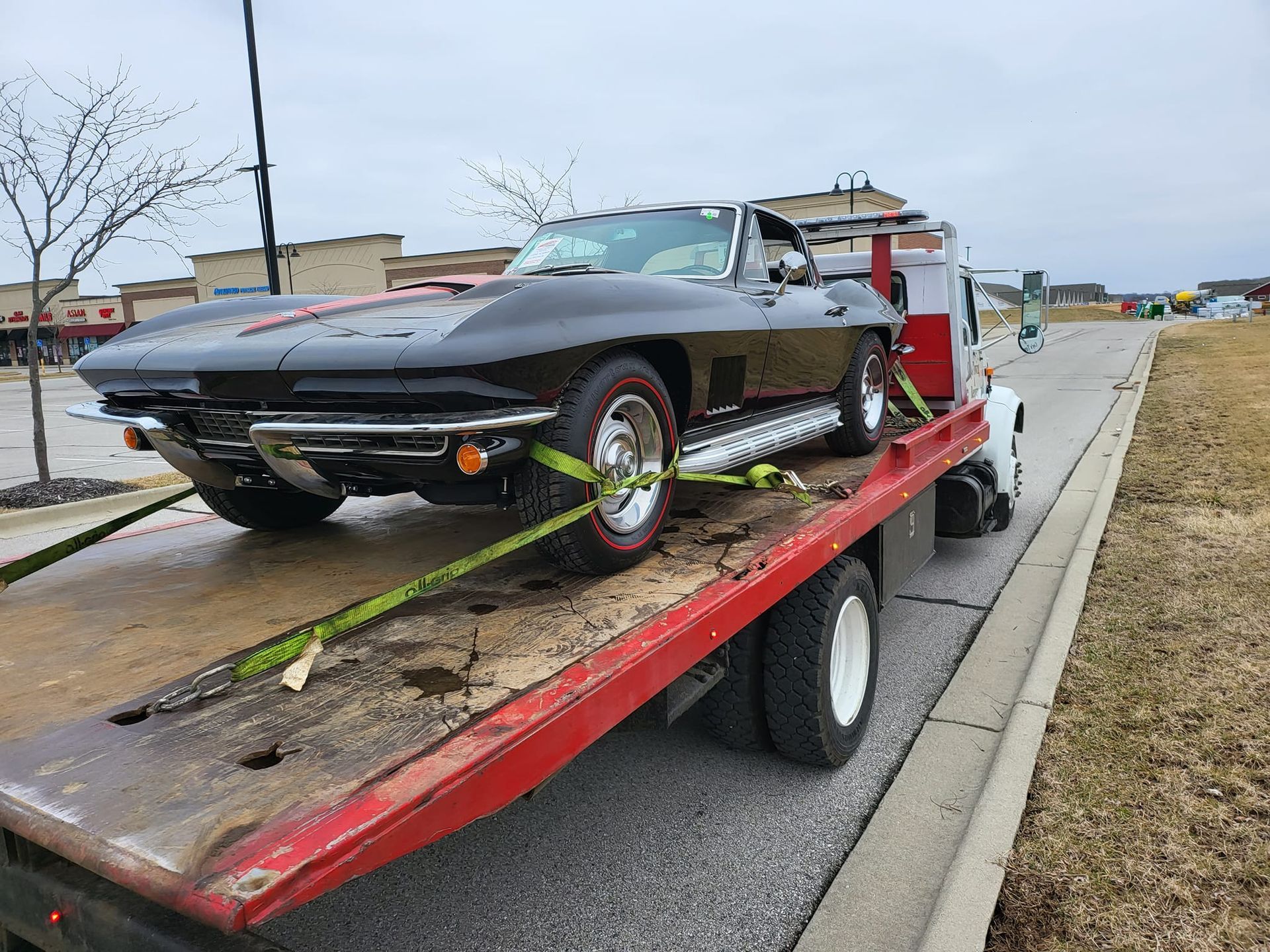 A black corvette is sitting on top of a red tow truck.