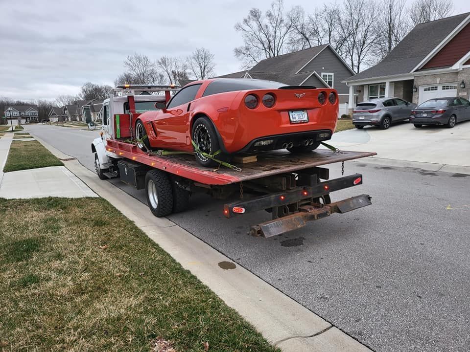 A red sports car is being towed down a street by a tow truck.