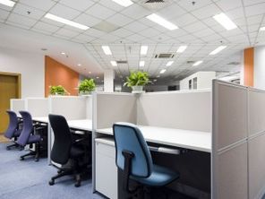 A row of cubicles in an office with chairs and tables.