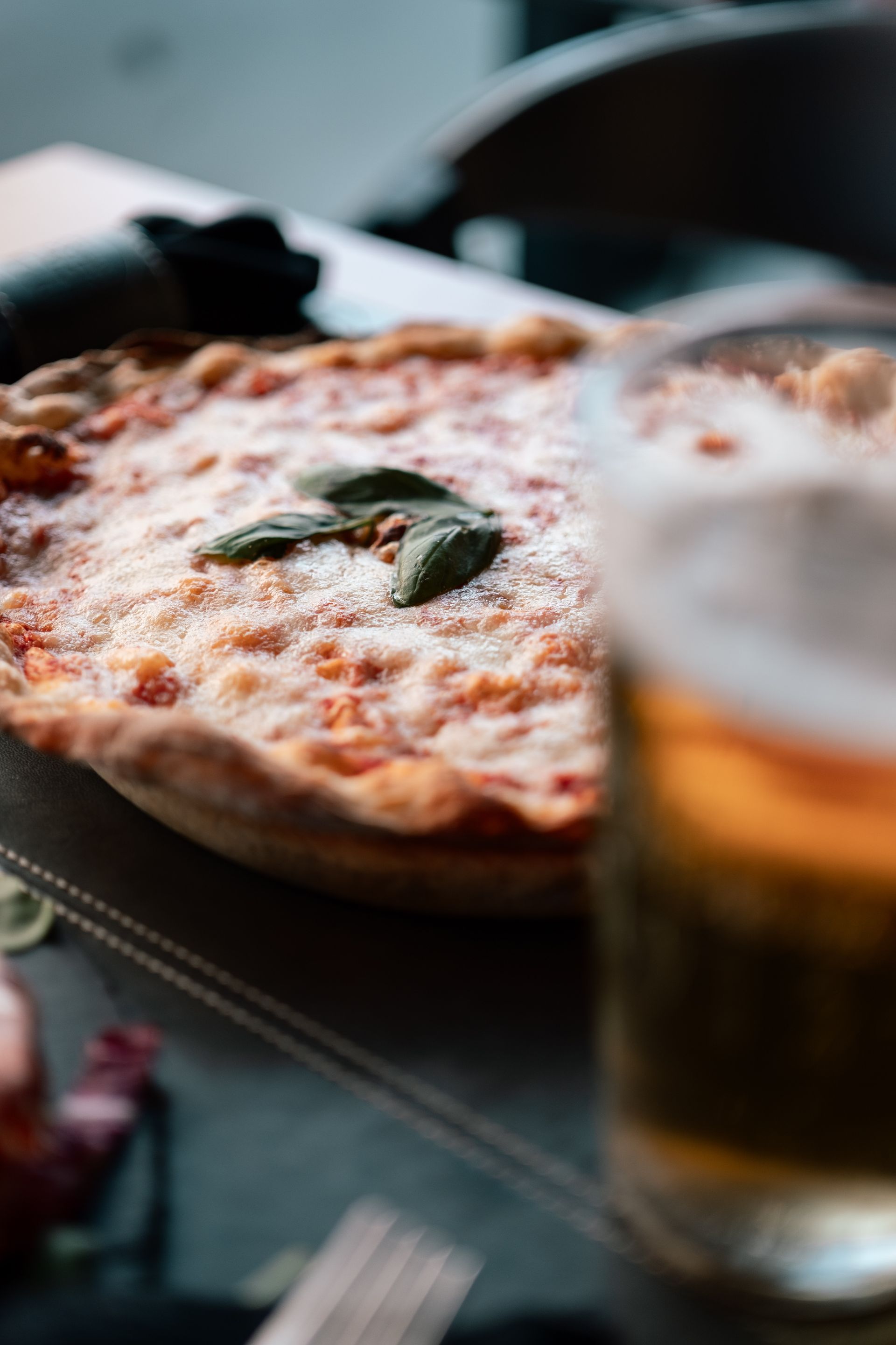 Una pizza su un tavolo con un bicchiere di birra in primo piano.