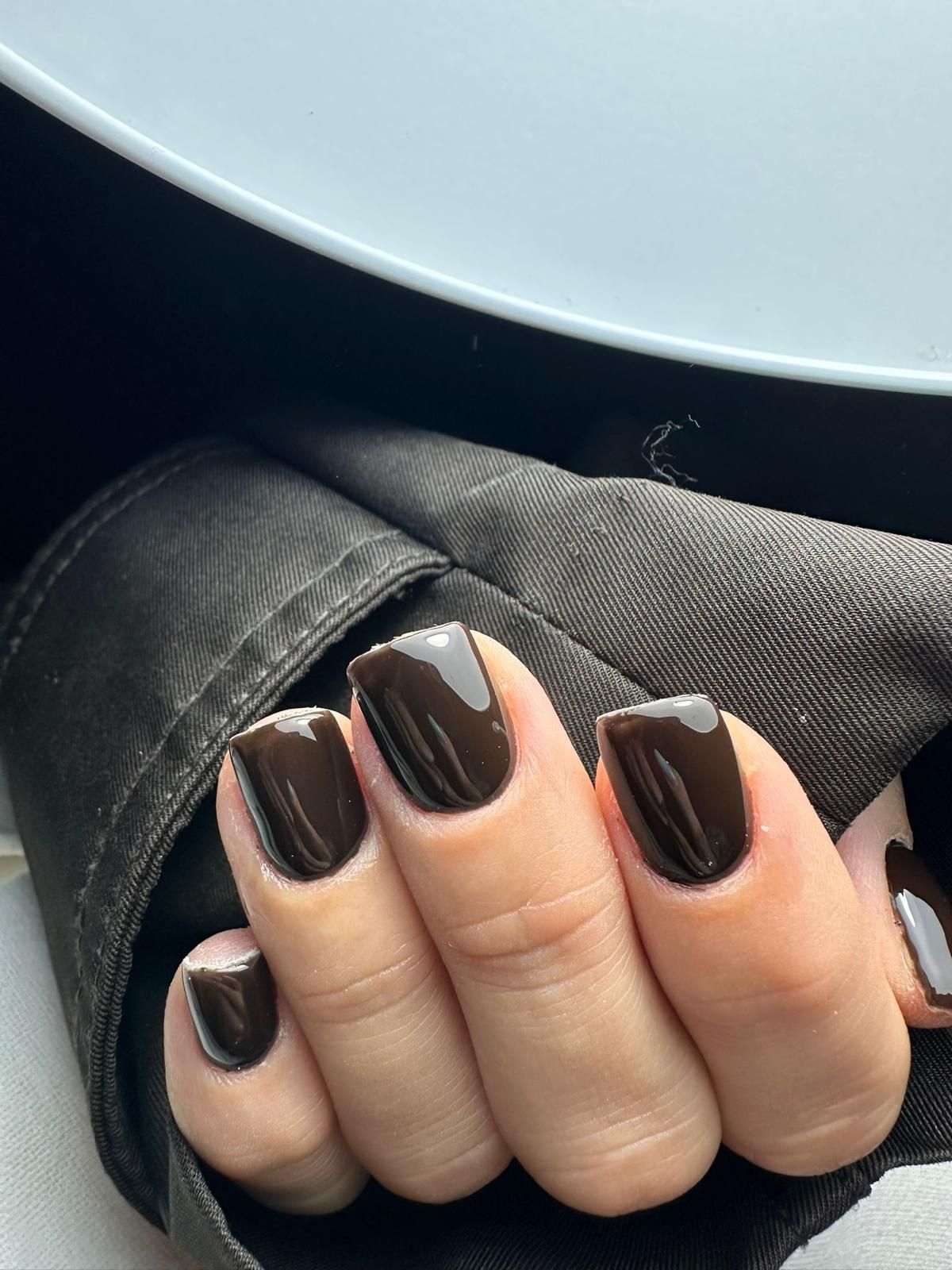Mano con unghie quadrate e smaltate color marrone scuro, appoggiata su un tessuto scuro.