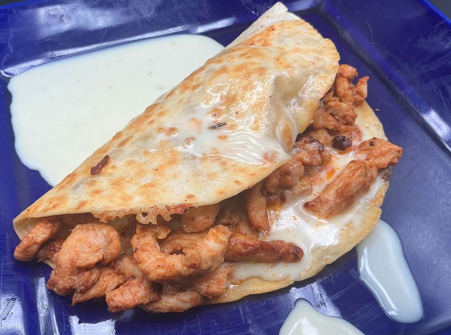 Quesadilla with chicken and cheese on a blue plate, served with white sauce.