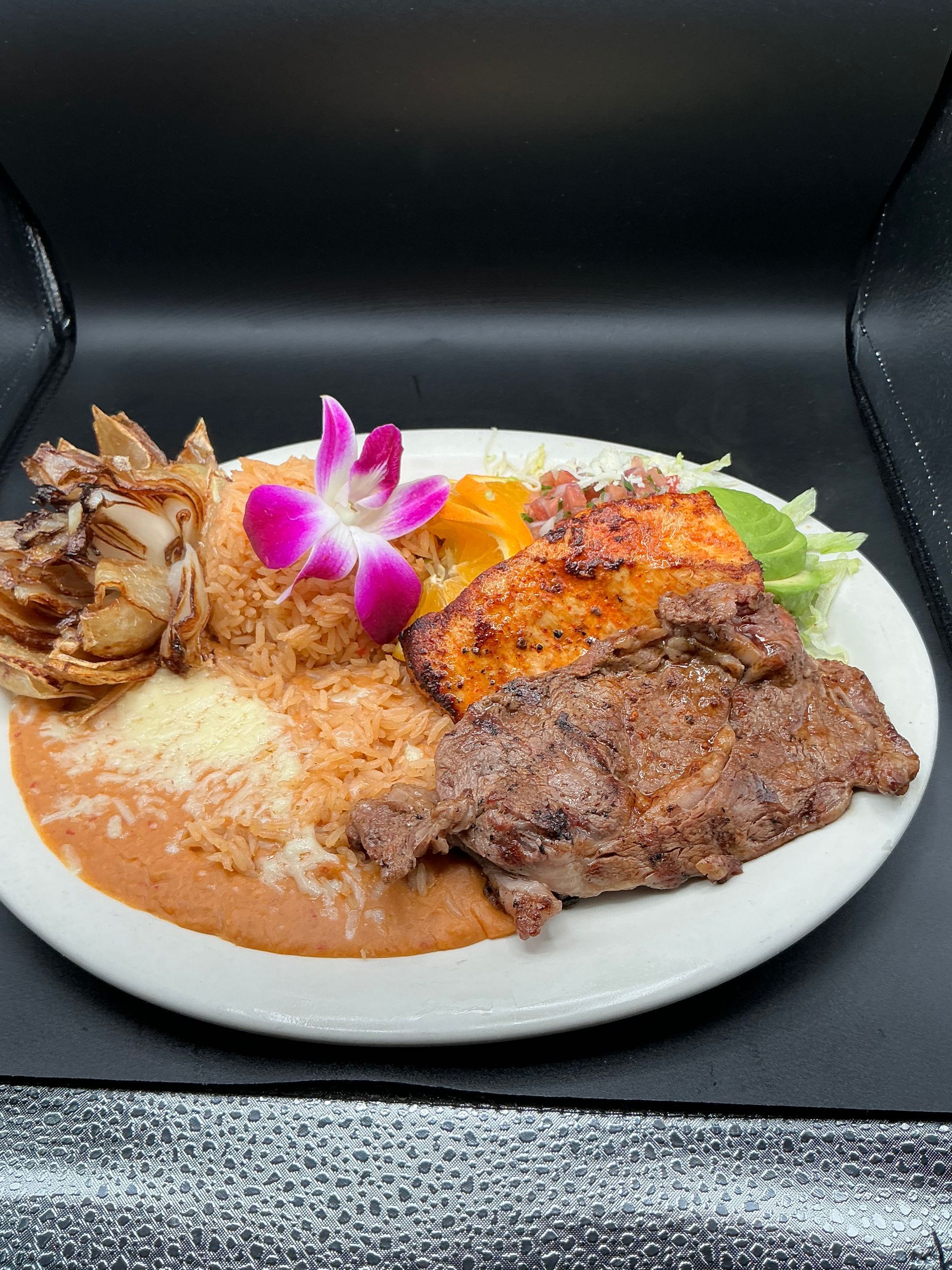 Plate of food with steak, salmon, rice, beans, lettuce, and flower garnish.