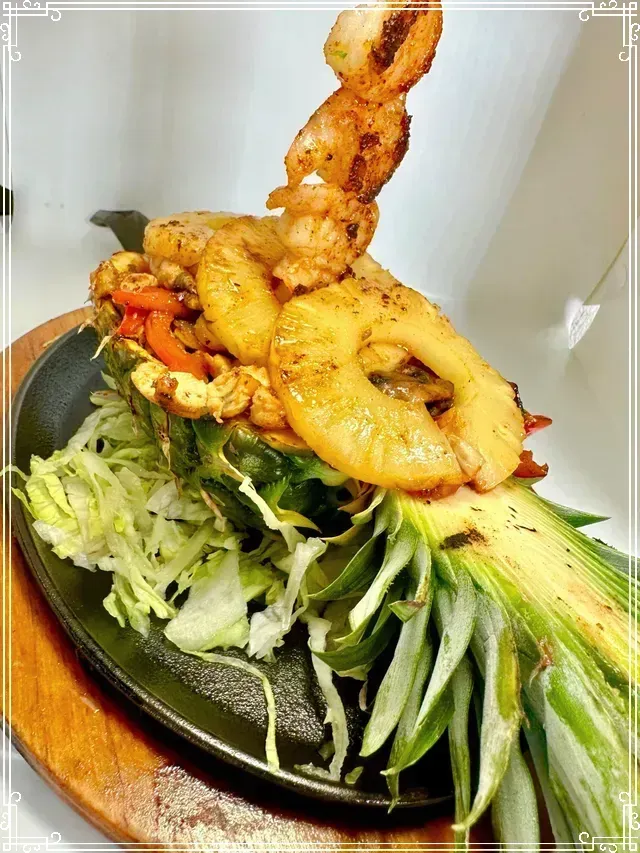 Tropical Fajitas, shrimp and vegetables in a pineapple boat, served on a sizzling plate with lettuce.