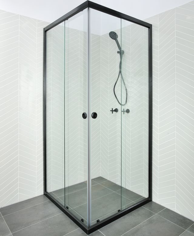 Black framed glass shower enclosure in a corner of a bathroom with a dark grey tiled floor and light grey chevron patterned wall — Cessnock Glass in Cessnock, NSW