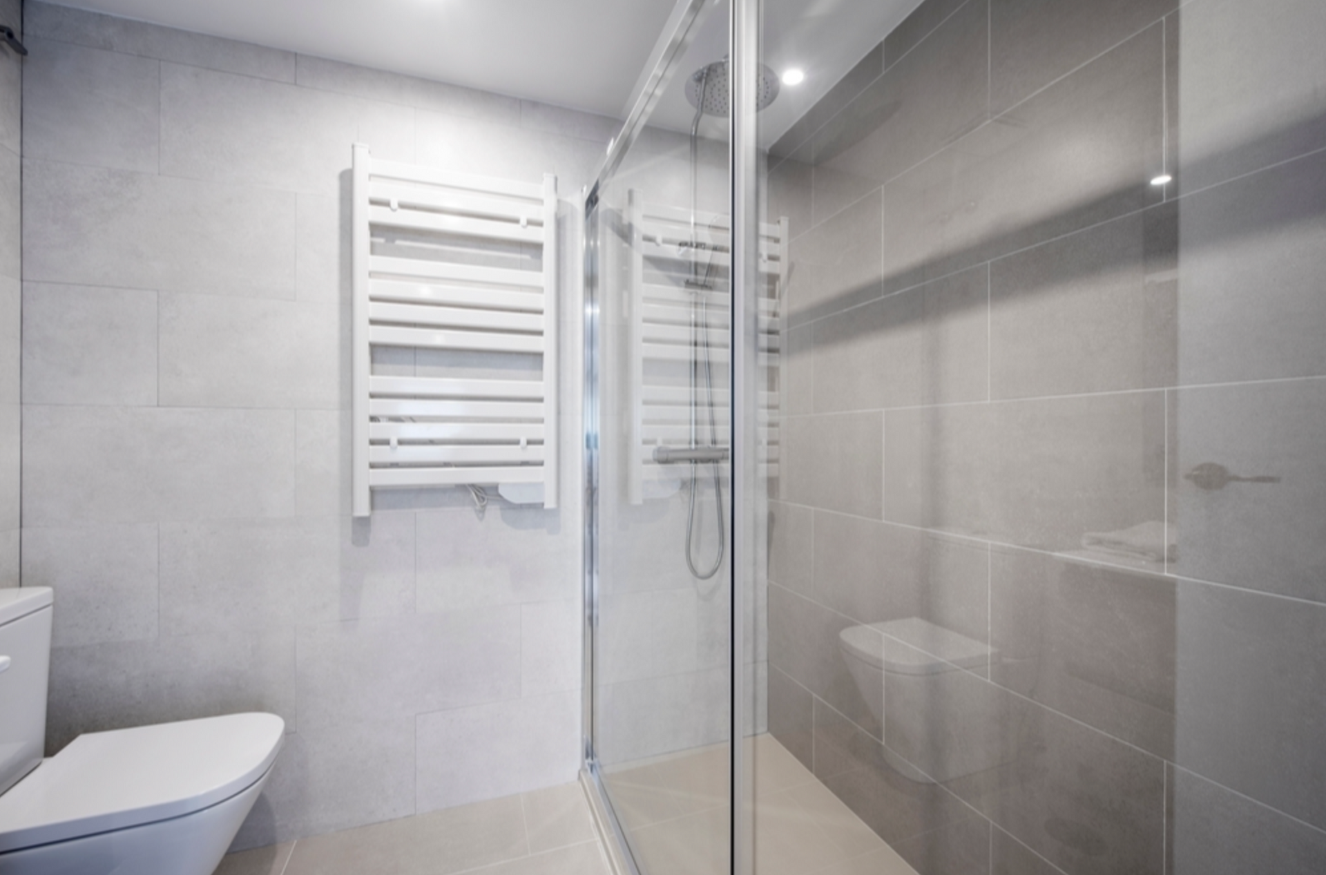 Bathroom with gray tiles, a glass shower, toilet, and a white towel warmer — Cessnock Glass in Cessnock, NSW