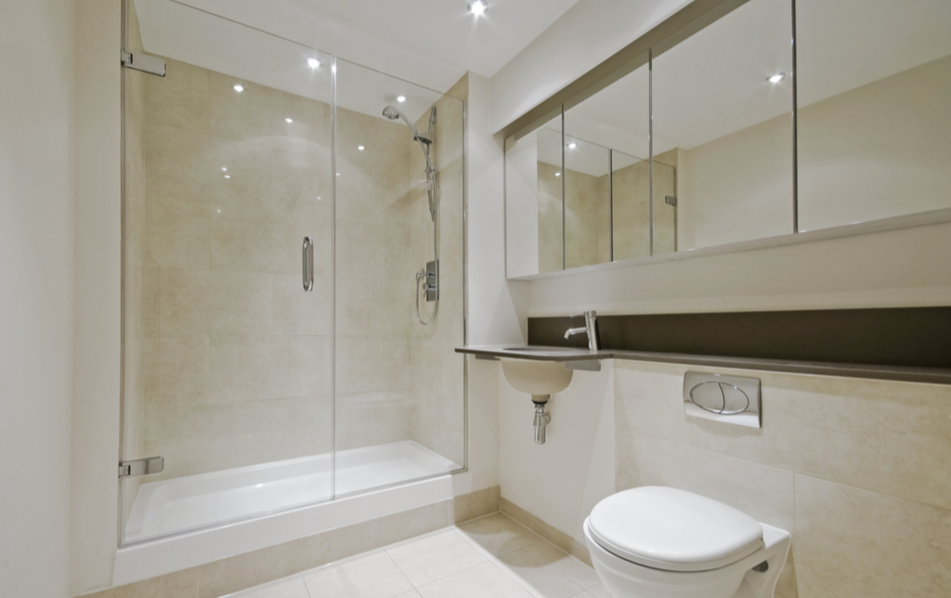 Modern bathroom with a glass shower, sink, and toilet. Beige tile walls and floor, bright lighting — Cessnock Glass in Cessnock, NSW