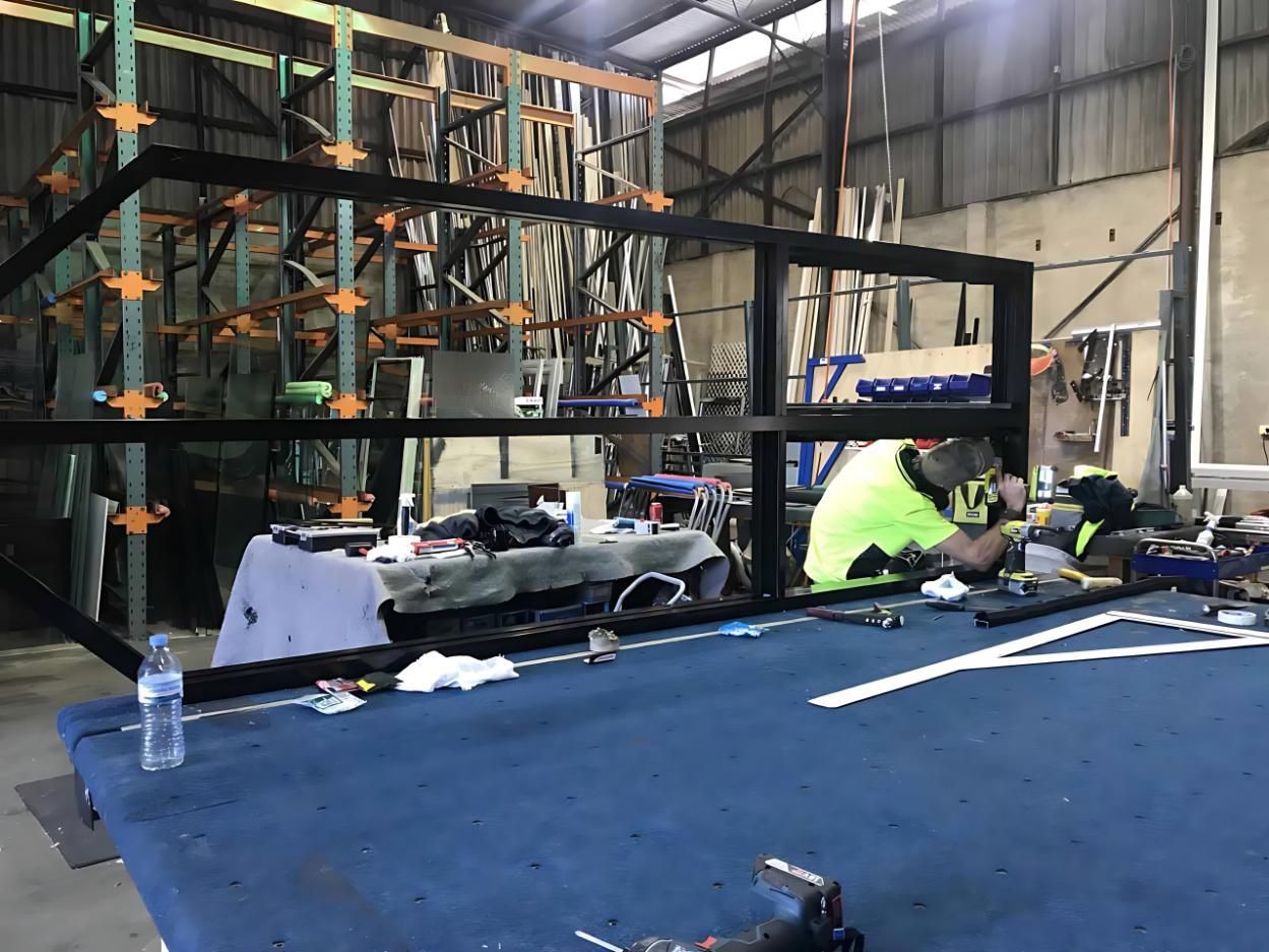 A Man is Working on a Piece of Metal in a Warehouse — Cessnock Glass in Cessnock, NSW