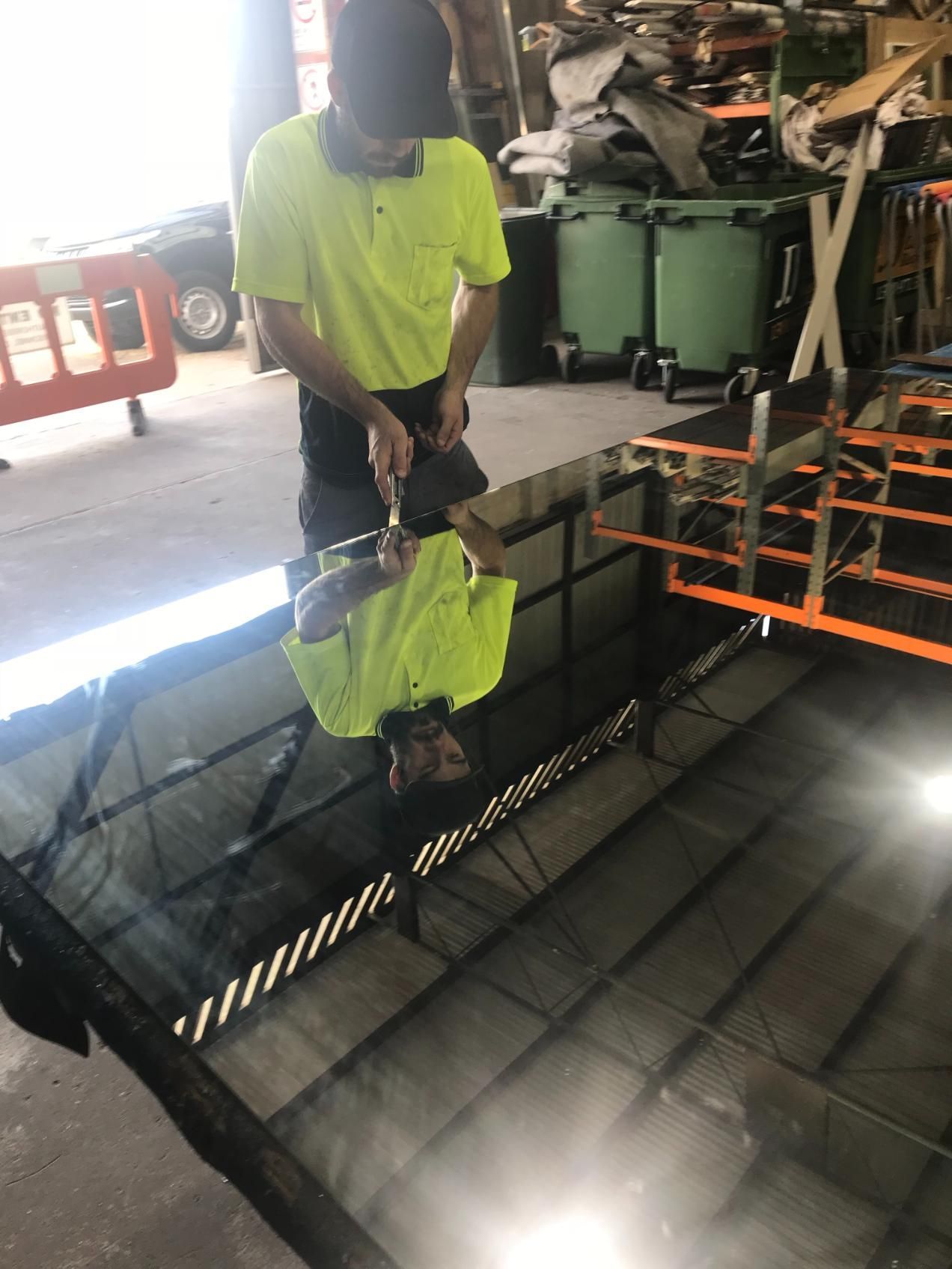 A person in a yellow shirt and black pants is working on a large, black, reflective surface — Cessnock Glass in Lake Macquarie, NSW