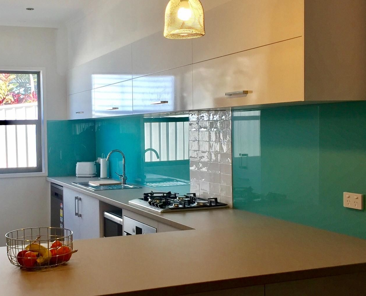 Modern kitchen with turquoise backsplash, stainless steel appliances, and a fruit basket on the counter — Cessnock Glass in Cessnock, NSW