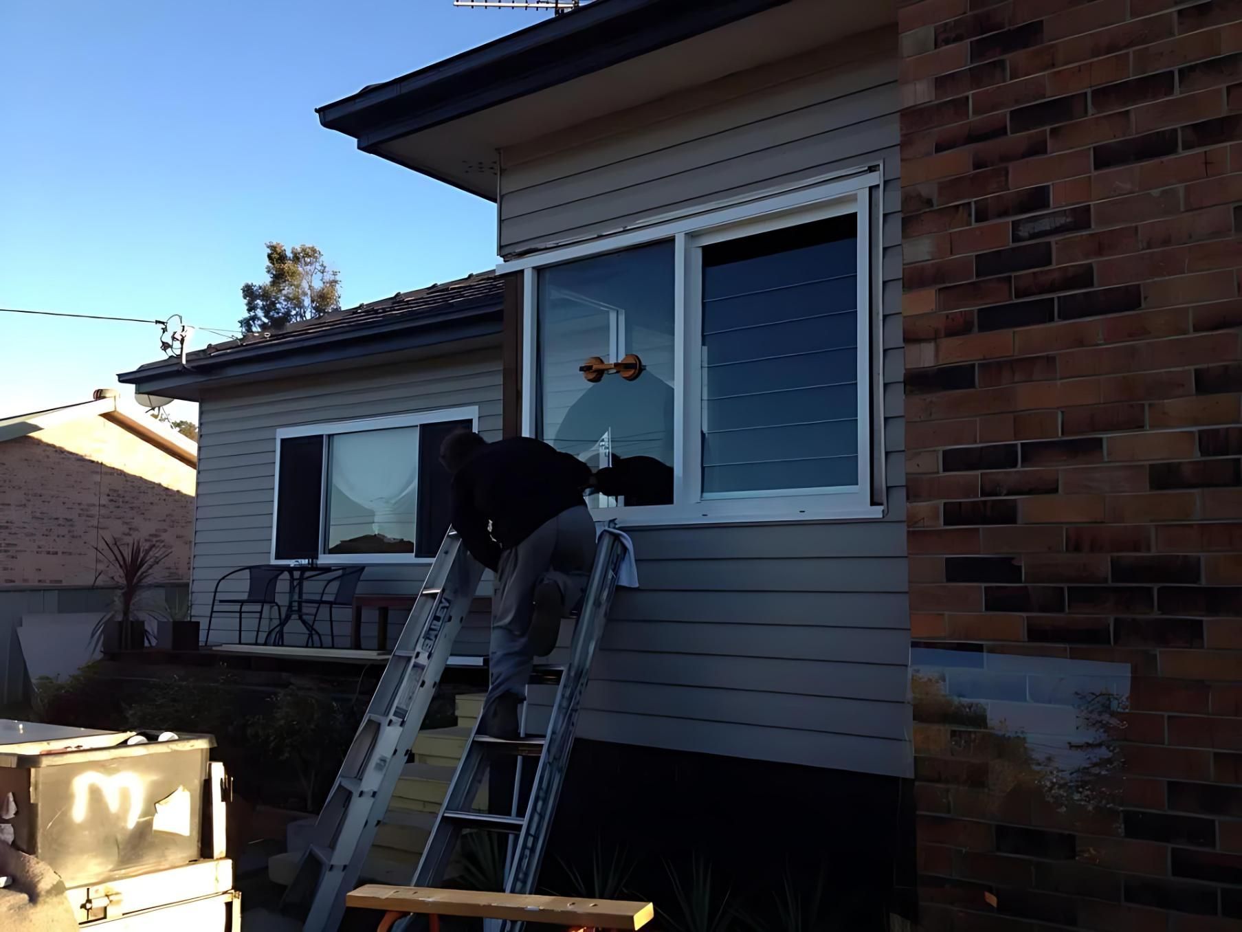 A Man on a Ladder is Working on a Window on the Side of a House — Cessnock Glass in Hunter Valley, NSW