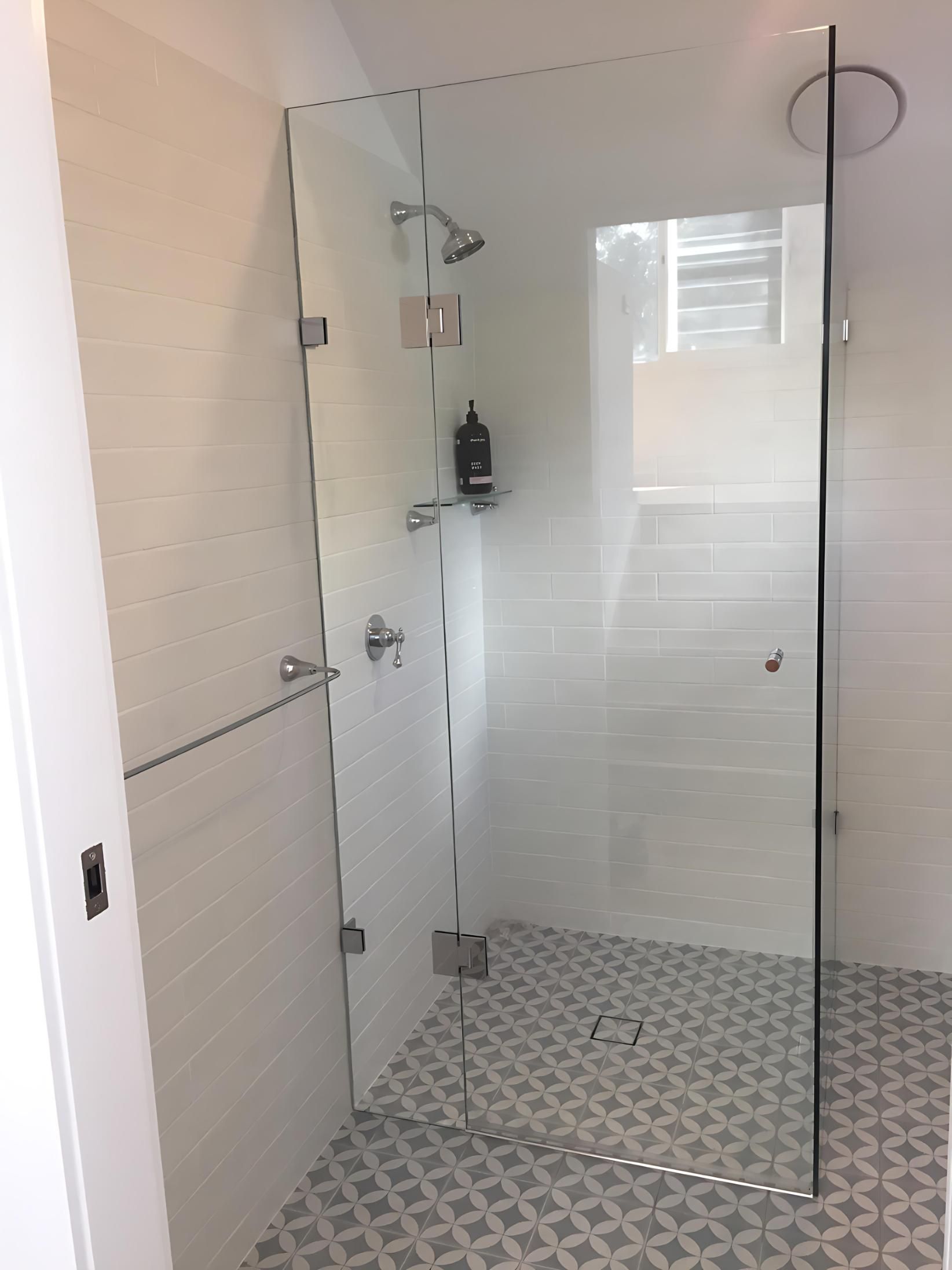 A glass shower screen with a shower with white tiles around the edge and pink tiles on the floor — Cessnock Glass in Central Coast, NSW