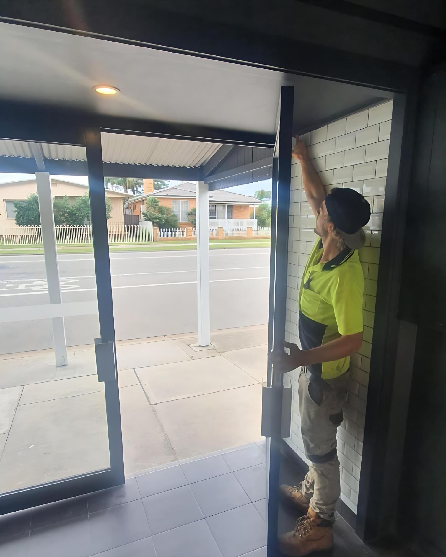 A Man in a Yellow Shirt is Standing in Front of a Glass Door — Cessnock Glass in Central Coast, NSW