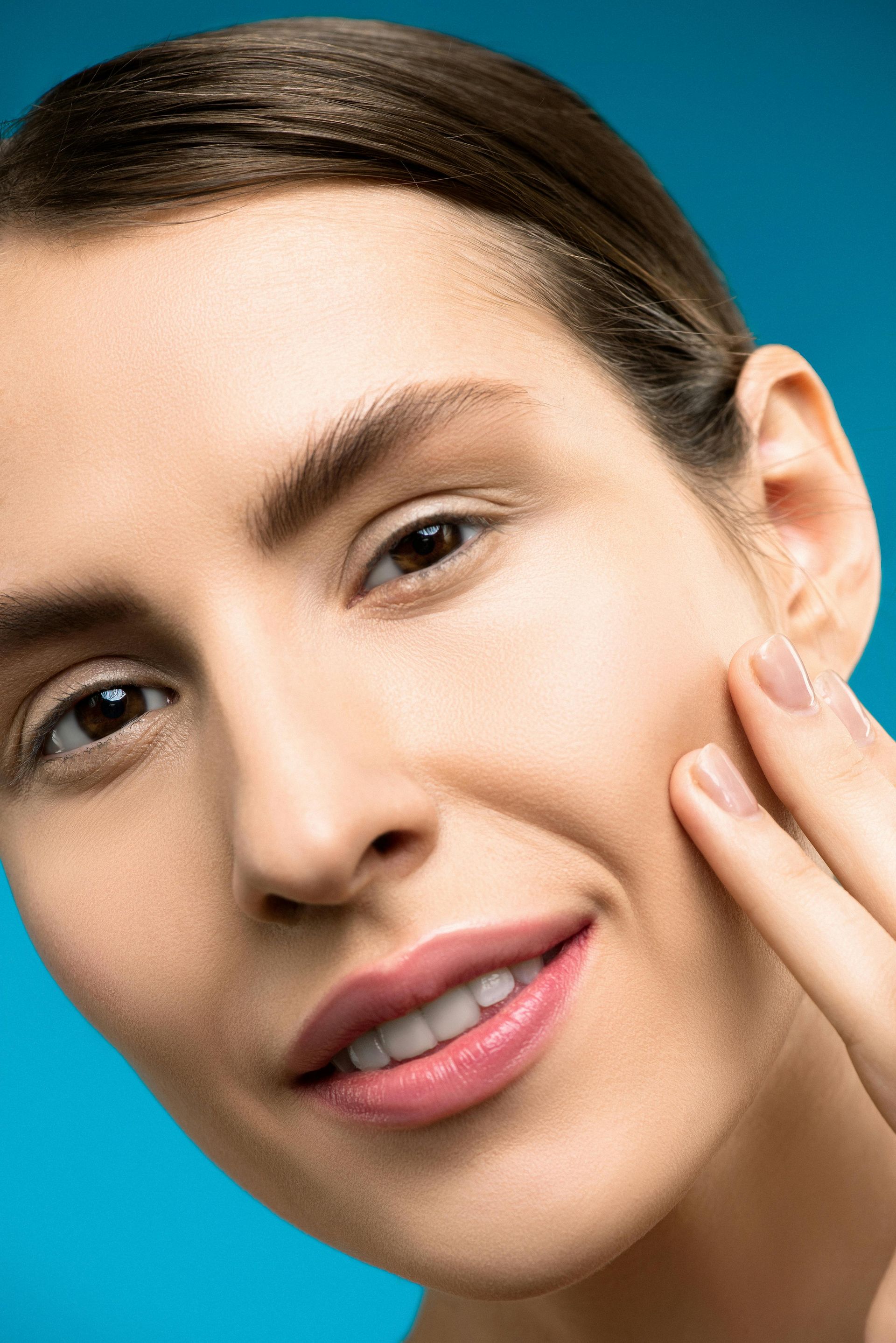 Woman touching cheek, smiling, against a blue background.