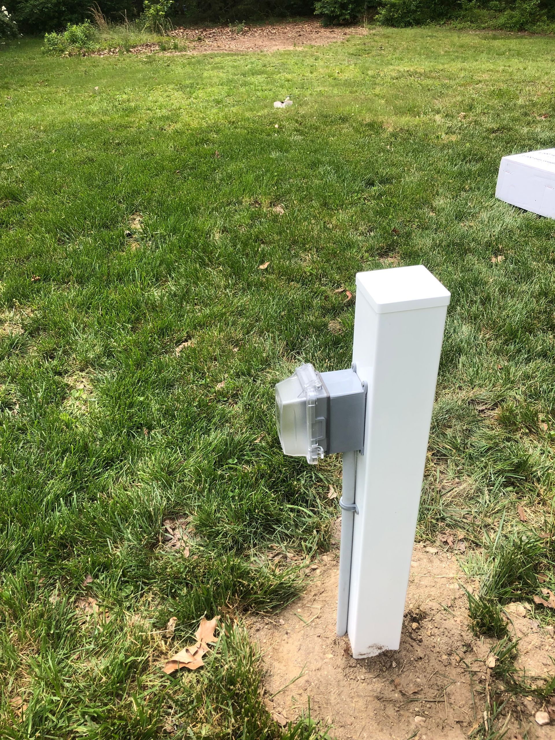 A white pole with a light attached to it is in the middle of a lush green field.