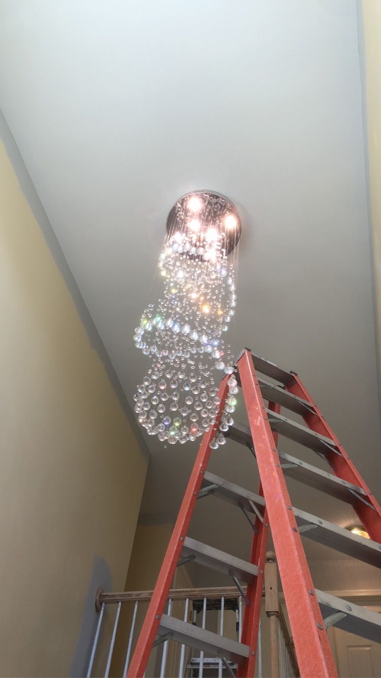 A ladder is sitting next to a chandelier hanging from the ceiling.