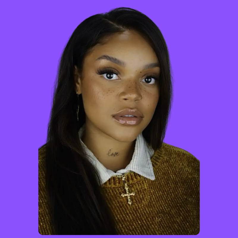 A woman with a tattoo on her neck is wearing a brown sweater with a cross necklace.