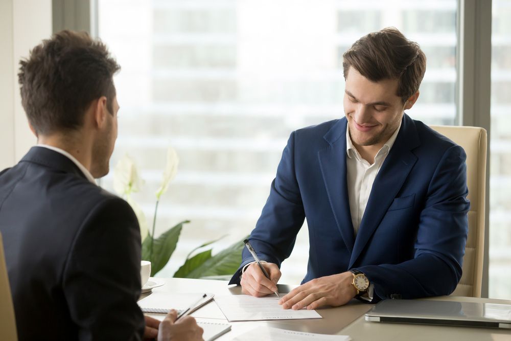 Smiling businessman signing paper at meeting — Employment Law Solicitors in Muswellbrook NSW