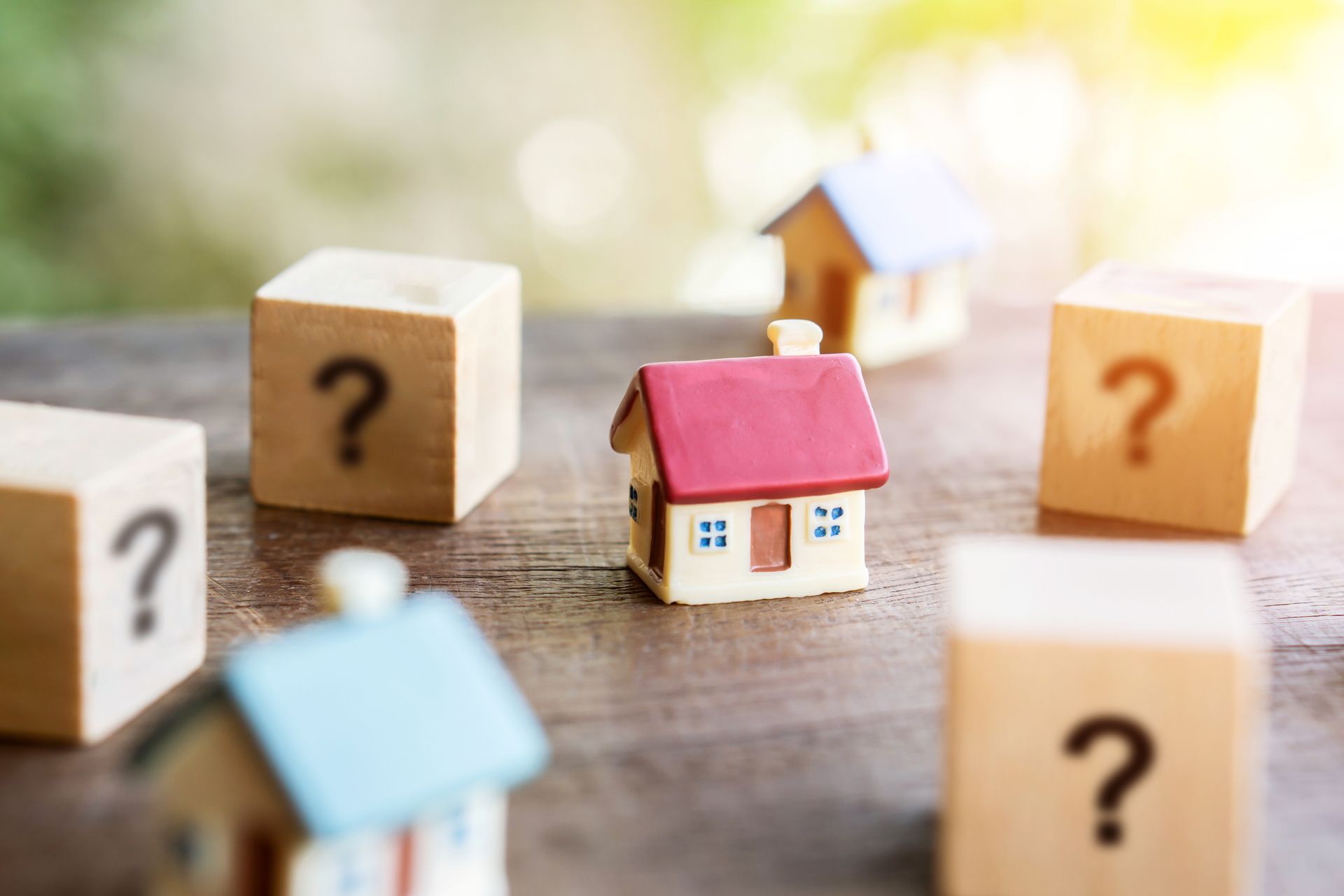 Miniature house surrounded by wooden blocks with question marks.