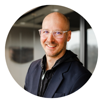 A bald man wearing glasses and a jacket smiles for the camera