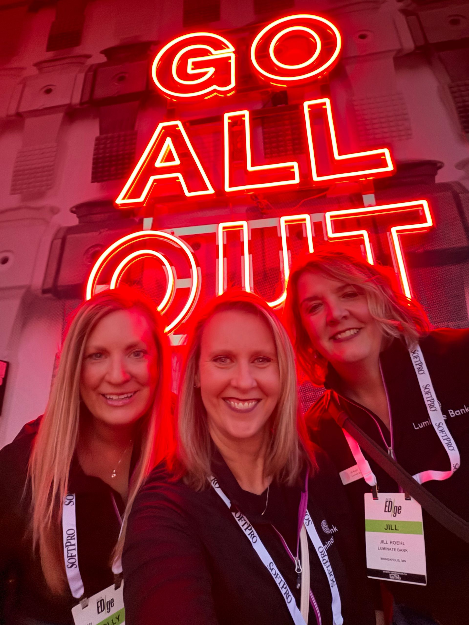 Four people smile on a golf cart, one driving. Sunny day, blue sky.
