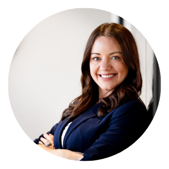 A woman in a blue jacket is smiling with her arms crossed