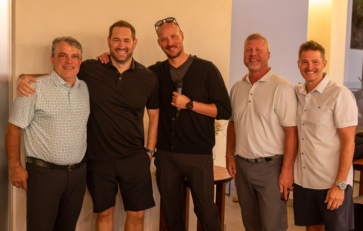 Group of people posing in front of an ancient stone building and a castle under a sunny sky.
