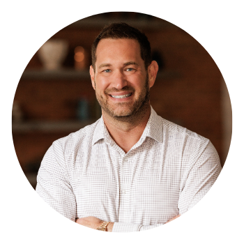 Man in a blue suit smiles, arms crossed, in an office setting.