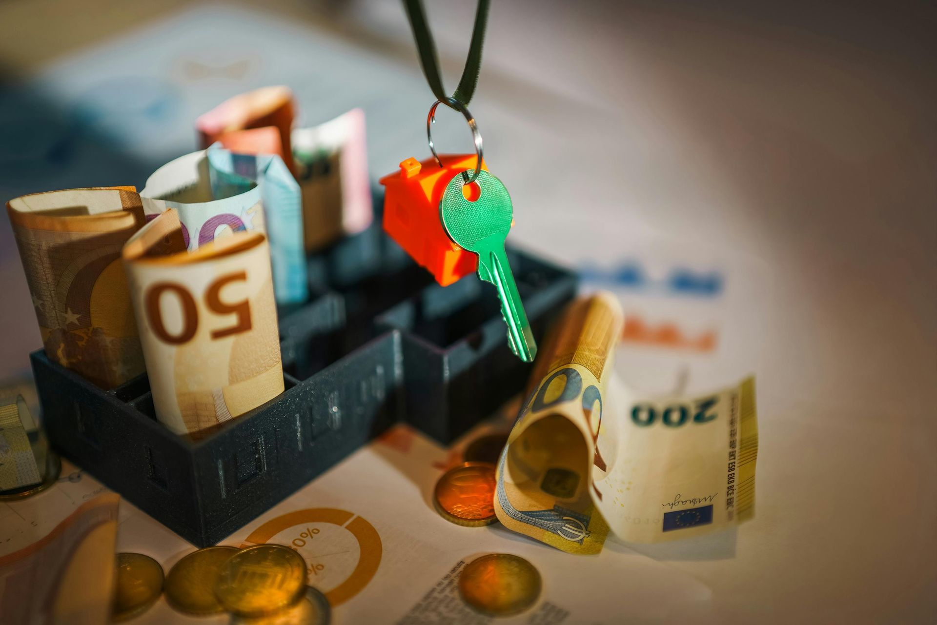 Black box filled with rolled Euro bills and coins. A green key hangs above the box.