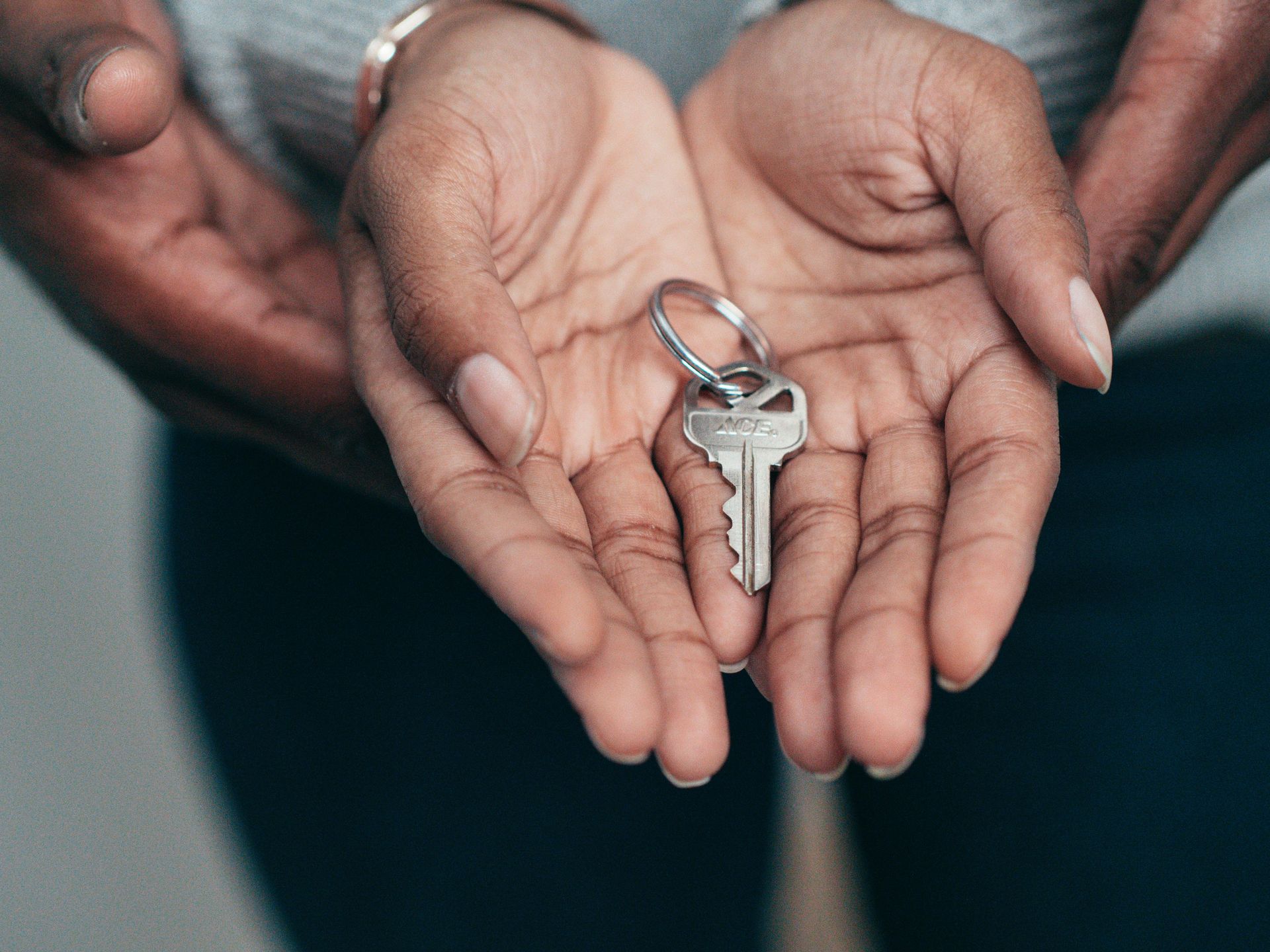 Two pairs of cupped hands held together, cradling a single silver house key on a metal ring.