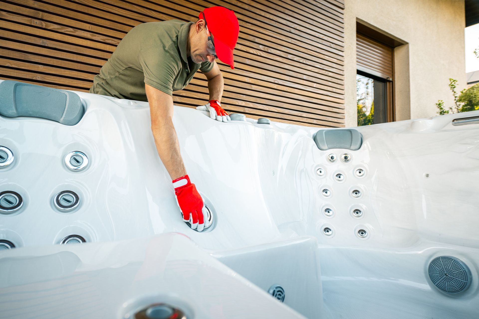 Person in red cap and gloves servicing a white hot tub, outdoor setting. Person in red cap and gloves servicing a white hot tub, outdoor setting.