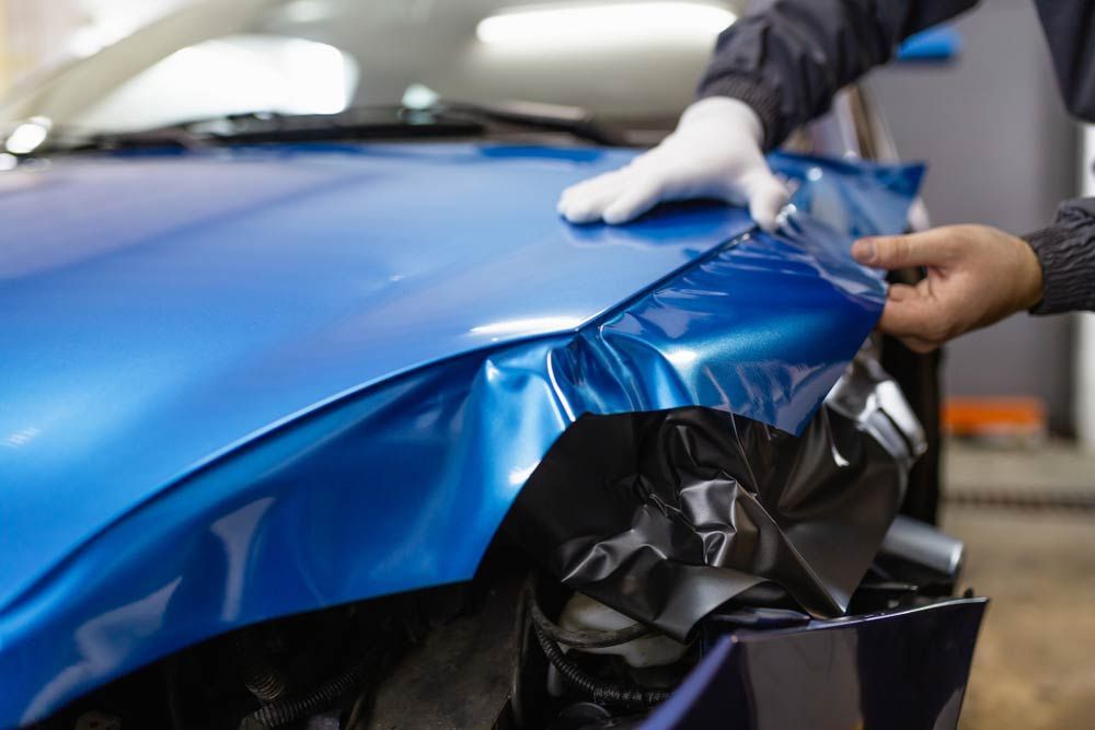 Worker Wrapping A Car With Blue Car Film — DNA Signs in Burleigh Heads, QLD